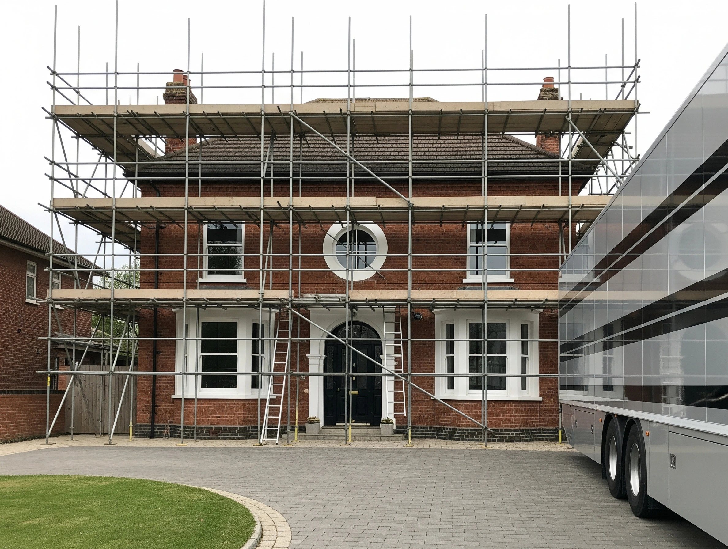 Red brick two-story house fully covered in scaffolding for construction or renovation.