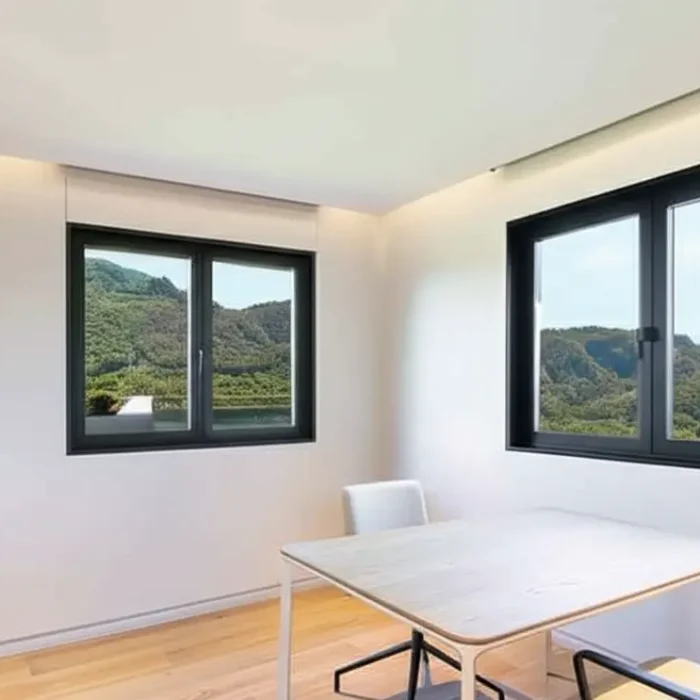 Minimalist interior with black-framed windows overlooking green, mountainous scenery.